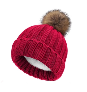 Detailed view of red knitted beanie with thick warm white fleece lining and brown pompom