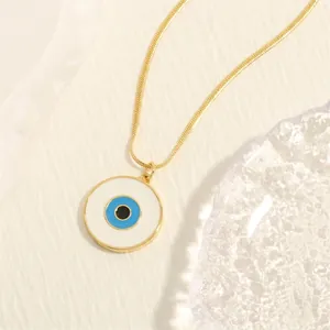 Close-up of golden snake chain with blue evil eye enamel pendant on white fabric