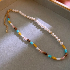 Detail of baroque pearl and multicolored crystal bead necklace with gold clasp on velvet tray