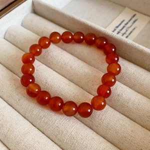 Macro shot of 8mm red agate beaded bracelet displayed in a cream velvet jewelry tray
