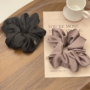 Detail of silk satin scrunchies in black and mocha with a gold logo tag on a tray