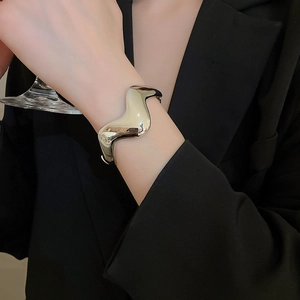 Detail shot of the polished wave-shaped cuff bracelet on a model wearing a black blazer