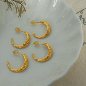 French vintage C-shaped gold hoop earrings with hammered honeycomb texture on white ceramic