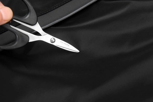 Close-up of black handle stainless steel scissors cutting through black fabric material