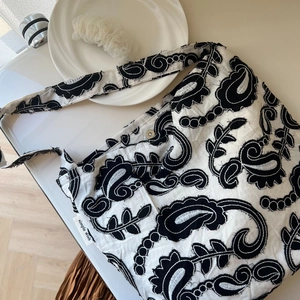 Close-up of black paisley embroidery and magnetic buckle on cotton linen shoulder bag