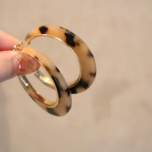 Detailed view of large C-shaped resin earrings with tortoise shell pattern and gold backing