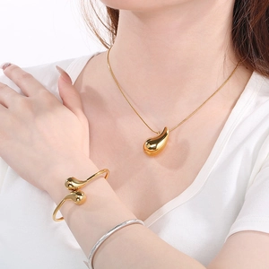 Detail of golden teardrop pendant necklace and open cuff bracelet on female model