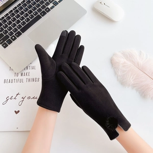 Detail of black touchscreen gloves featuring a fur pom-pom and split cuffs on a desk