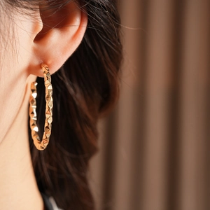 Close-up of golden geometric C-shaped hoop earring on model showing metallic texture