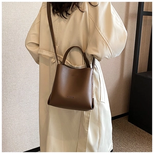 Detail view of a vintage brown leather bucket bag worn with a stylish trench coat