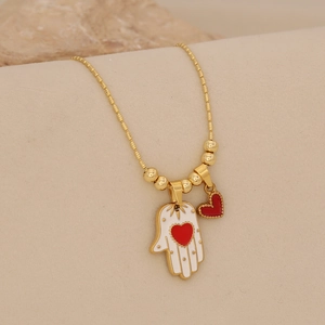 Detail of Hamsa Hand and heart charm on a golden bead chain necklace displayed on beige stand