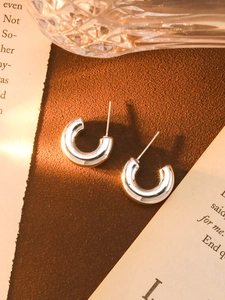 Close-up of silver C-shaped acrylic earrings on a vintage desk with warm natural lighting