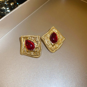 Detail of vintage gold earrings with embossed patterns and deep red oval gemstones