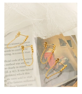 Macro detail of gold tassel chain earrings with twisted bar on artistic vintage background