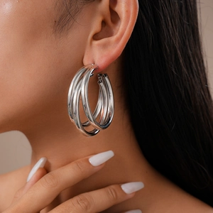 Close-up of silver geometric multi-layer C-shaped hoop earrings worn by a model