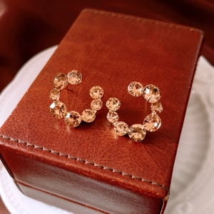 Macro détaillée de boucles d'oreilles en C serties de cristaux sur boîte en cuir luxe