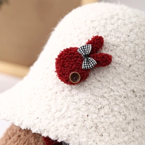 Close-up of white plush lamb wool bucket hat with red bunny and houndstooth bow detail
