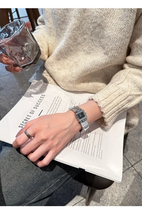Détail d'une montre carrée argentée au cadran noir avec une bague en argent entrelacée
