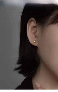 Gros plan sur des boucles d'oreilles cubes en argent S925 doré portées par un mannequin