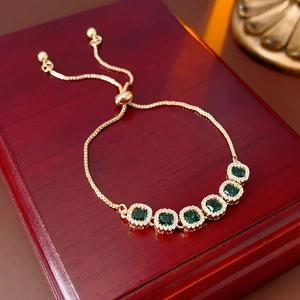 Detailed close-up of gold bracelet featuring square green gemstones on a wooden box
