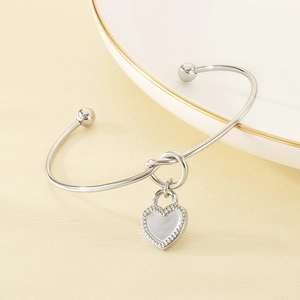 Detail of silver knot cuff bracelet with white heart pendant on elegant porcelain plate