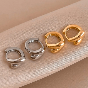 Minimalist twisted metal hoop earrings in gold and silver set on beige velvet surface