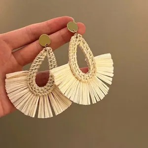 Detail of fan-shaped beige raffia woven earrings with golden metal studs in hand