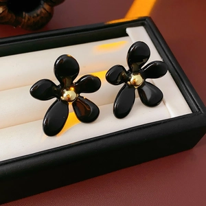 Macro shot of black flower earrings with gold centers on a soft jewelry cushion
