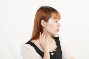 Close-up of golden woven floral stud earrings worn by a model in minimalist style