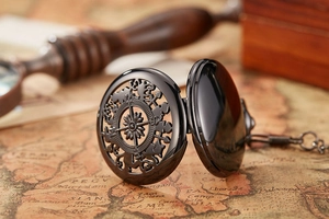 Close-up of black hollow pocket watch with compass relief on vintage map background