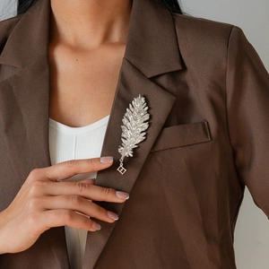 Detail of a vintage silver feather brooch with a geometric pendant on a brown suit jacket