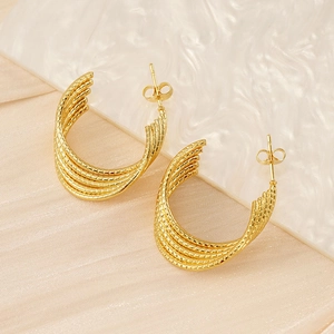 Detailed close-up of golden multi-layer twisted hoop earrings on marble surface