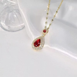 Elegant gold necklace with a red teardrop pendant and micro-set crystals on white silk