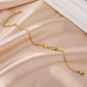 Detailed close-up of a gold 'Mama' charm bracelet on a soft champagne silk fabric