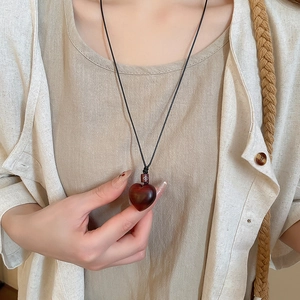 Detail of a handmade wooden heart pendant on a black cord necklace worn by a model