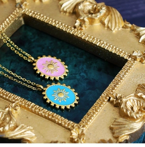 Macro detail of Bohemian oval sunburst pendants in pink and blue enamel on gold chains