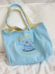 Blue canvas tote bag with cake embroidery and yellow checkered straps in flat lay view