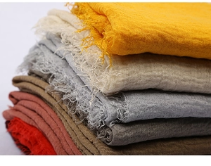 Close-up of stacked colorful voile scarves featuring frayed edges and wrinkled texture