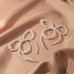 Detailed macro view of elegant pearl bow earrings resting on smooth champagne silk fabric