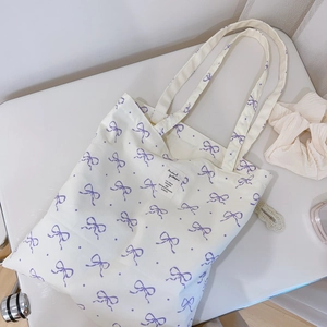 Close-up of white canvas tote bag with purple bow prints and woven label detail