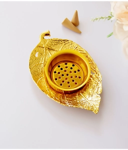 Detail of golden leaf-shaped metal incense burner with cone incense on a clean white surface