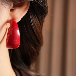 Macro side view of a large red C-shaped resin earring worn on a model for a chic look