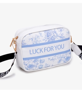 Detail of white floral camera bag featuring LUCK FOR YOU text and wide woven strap