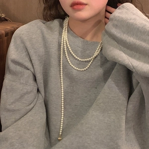 Long white pearl necklace with heart pendant layered on a grey sweatshirt