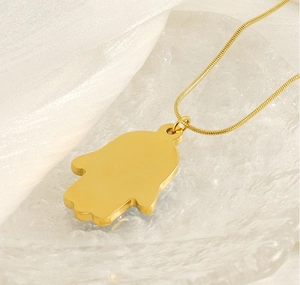 Detailed macro of golden Hamsa Hand pendant and snake chain on elegant silk surface