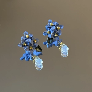 Detail of blue flower earrings with metal leaves and transparent teardrop pendants