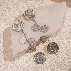 Macro detail of silver geometric round discs and long tassels on textured stone