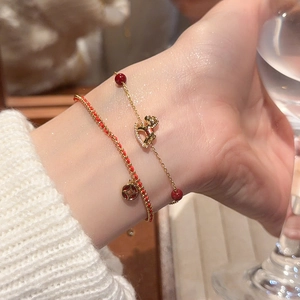 Detail of red cord bracelet with coin charm and gold chain with zircon horse pendant