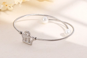 Detailed close-up of a silver steel wire bracelet with crown charm and pearl accents
