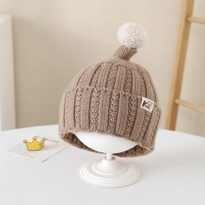 Close-up of brown knit baby beanie with white pompom on a wooden display stand